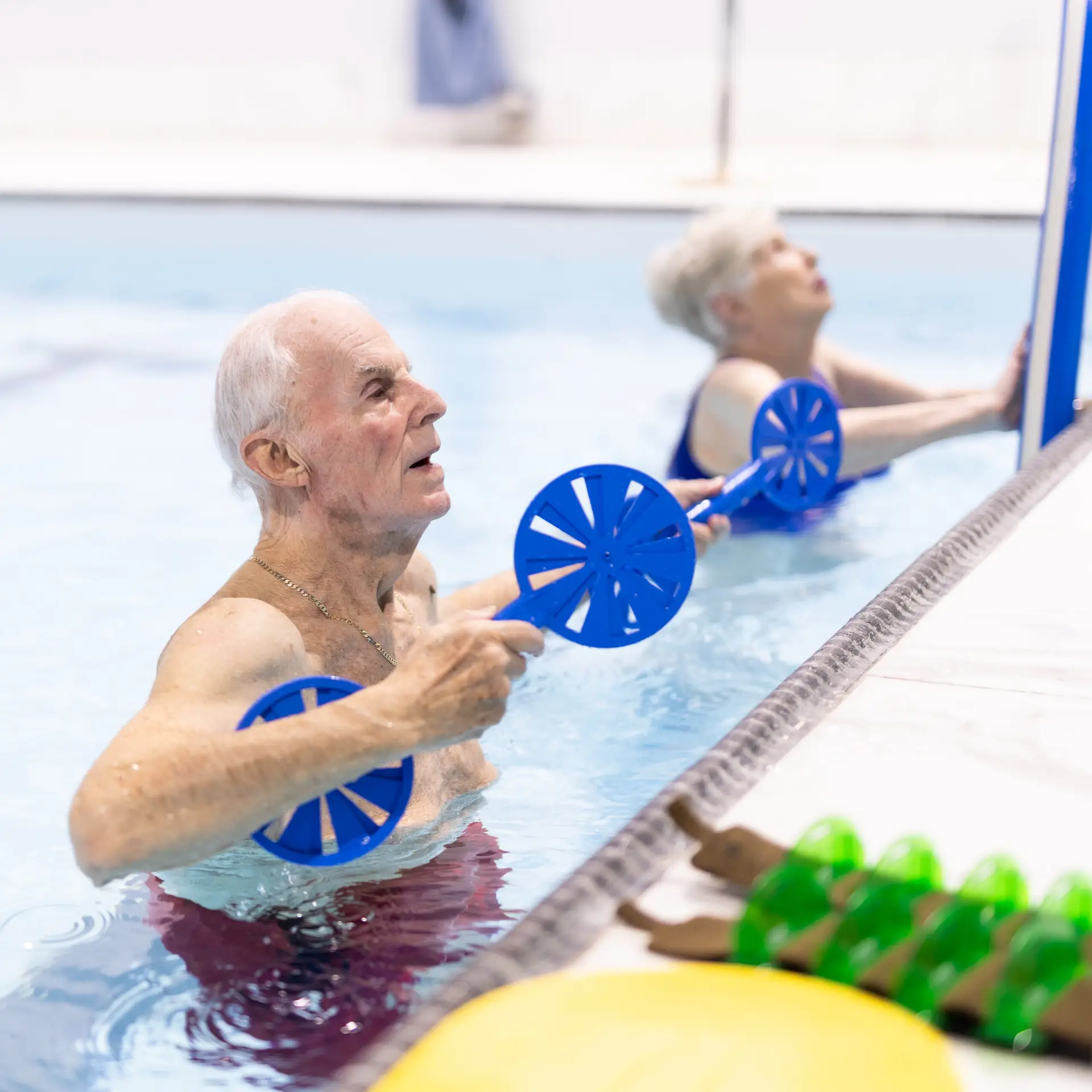 Senior man and woman participating in aqua therapy at HydroActive, using resistance paddles for mobility improvement and injury recovery.